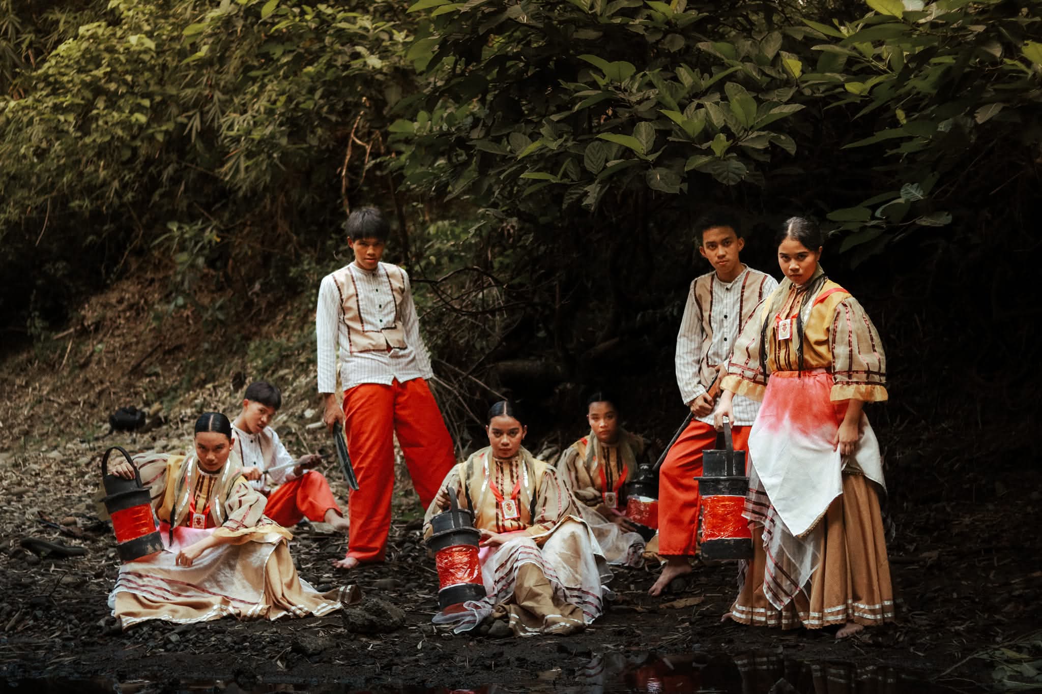 Performers resting beside a stream after the reenactment, holding lanterns.